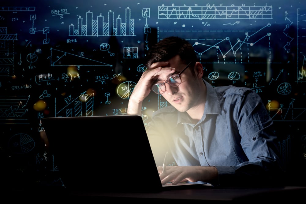 Young handsome businessman working late at night in the office with blue calculations in the background Young handsome businessman working late at night in the office with blue calculations in the background